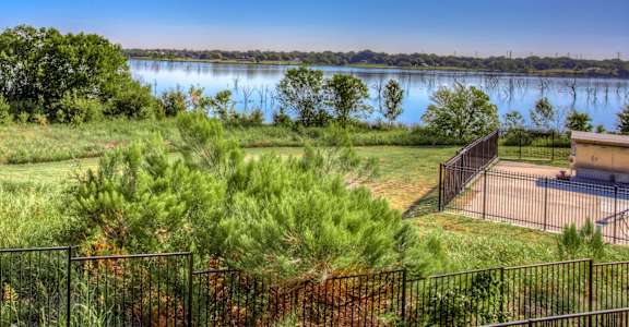 A view of a lake from a hill with a fence in the foreground.