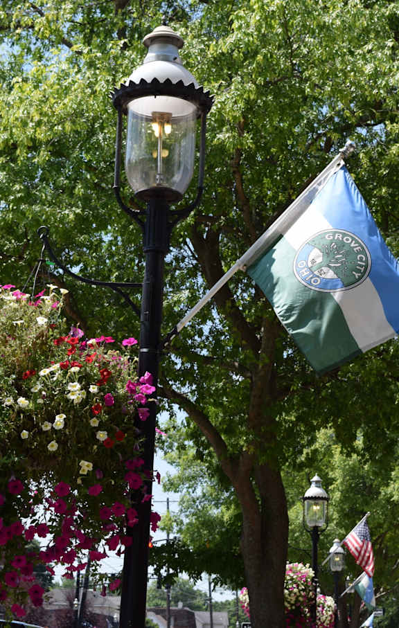 A street lamp with a hanging basket of flowers and a flag on a pole.