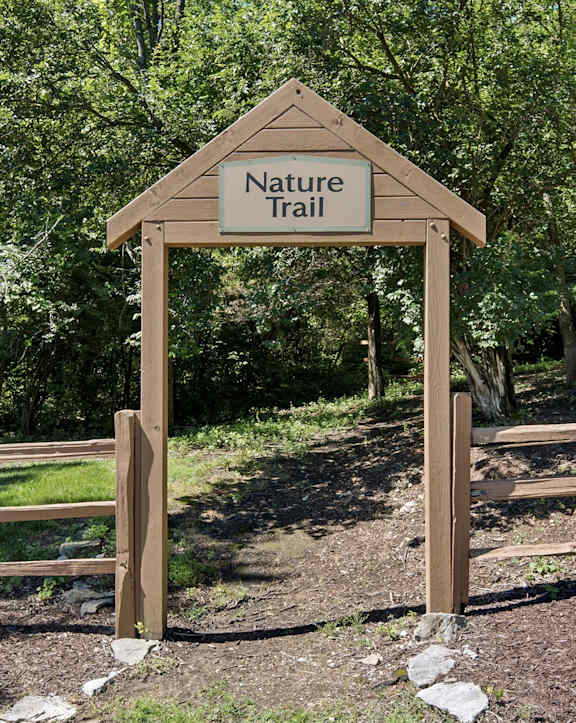A wooden Nature Trail sign stands in a grassy area.