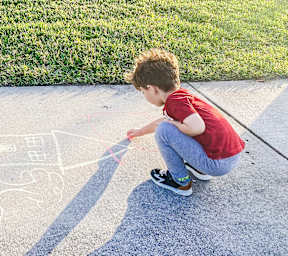 A boy drawing on the sidewalk with chalk.