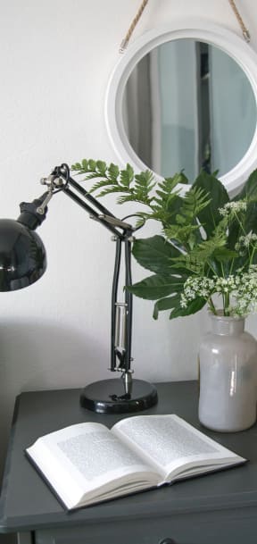 Grey dresser with open book, black lamp, grey vase with greenery, and grey mug.
