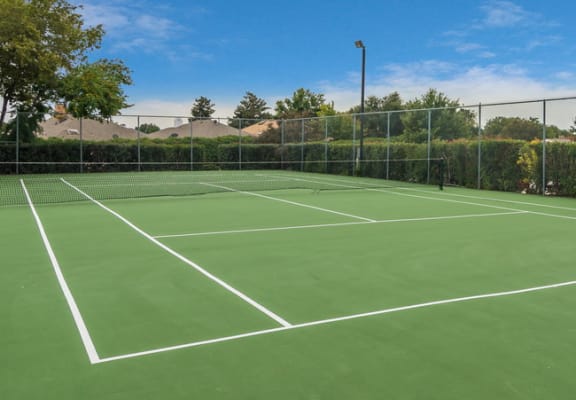a tennis court with green turf and a fence at Seacrest Apartments, Garland