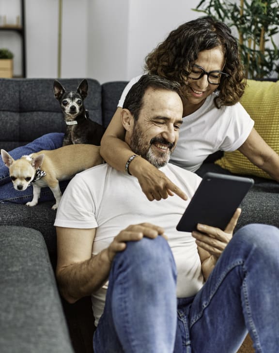 a couple sitting on a couch with their dogs and looking at a tablet