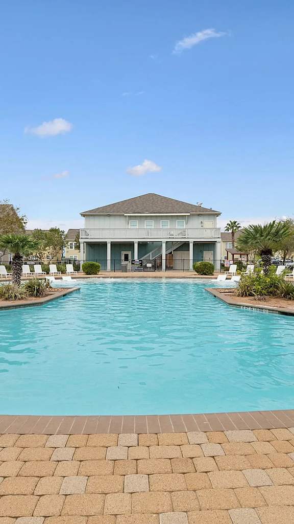 A large outdoor swimming pool surrounded by a brick patio and wooden pergolas.