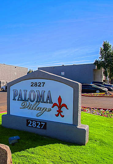 A sign for Paloma Village stands in front of a building.