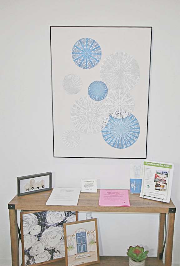 A table with a white and black floral table cloth and a framed picture of blue and white circles.