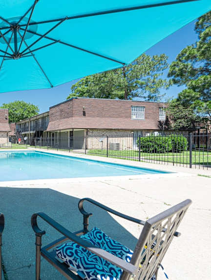 A pool area with chairs and a blue umbrella.