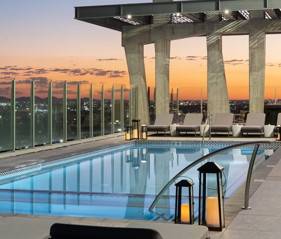 a swimming pool on the top of a skyscraper overlooking a city at dusk