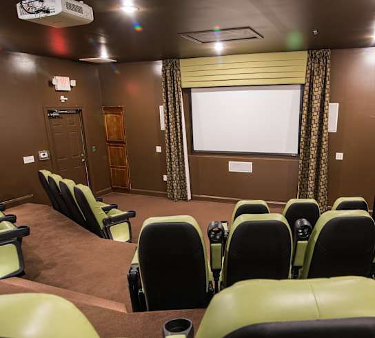 A row of green chairs are arranged in a room with a screen and projector.