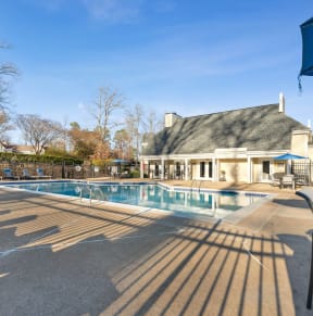 a swimming pool with chairs and umbrellas in front of a house