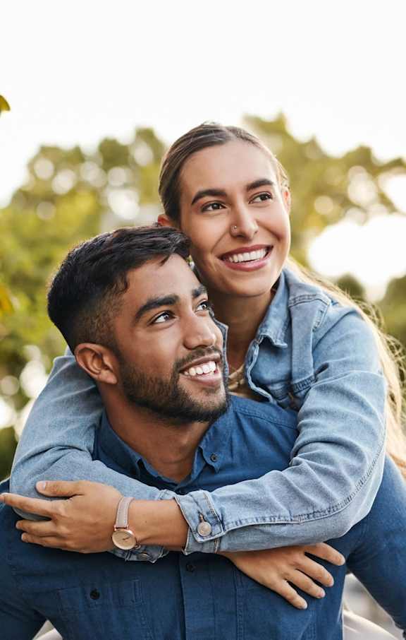 A man is giving a woman a piggyback ride in a park.