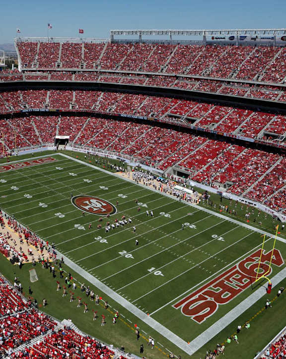 A stadium full of red seats with a football game taking place.