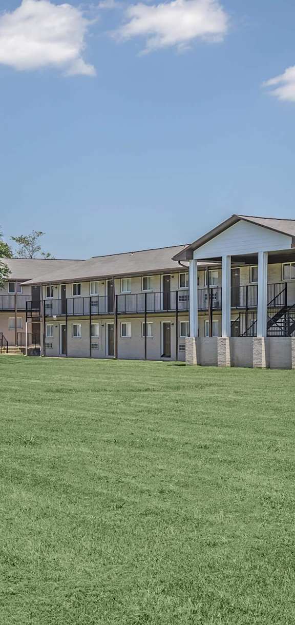 A large grassy field in front of a building with a tree in the middle.
