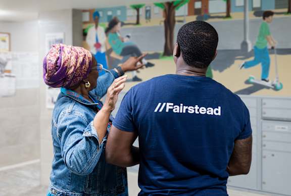 A man and a woman are standing in front of a mural with the hashtag #Fairstead on it.