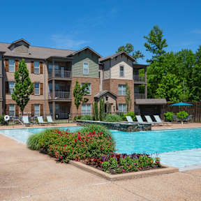 A large apartment complex with a pool and lounge chairs.