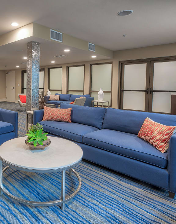 a resident clubhouse with blue couches and chairs and a coffee table with a potted plant