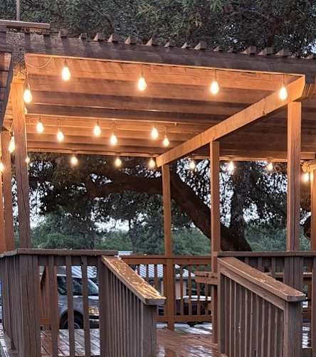A wooden gazebo with lights strung up is surrounded by trees.