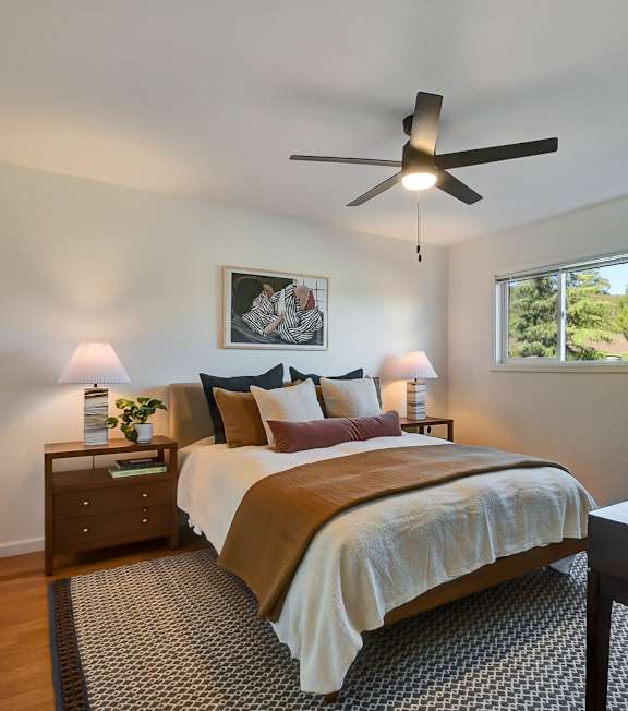 A bedroom with a bed, nightstand, and a ceiling fan.