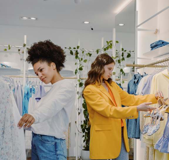 Two women shopping for clothes in a brightly lit store.