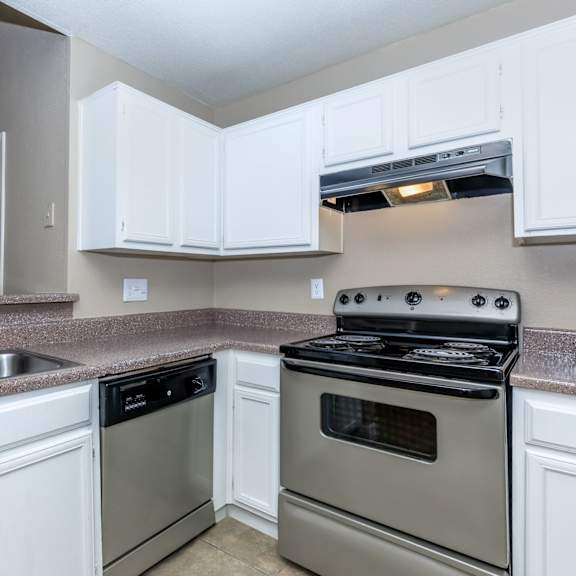 A kitchen with a stove, sink, and cabinets.