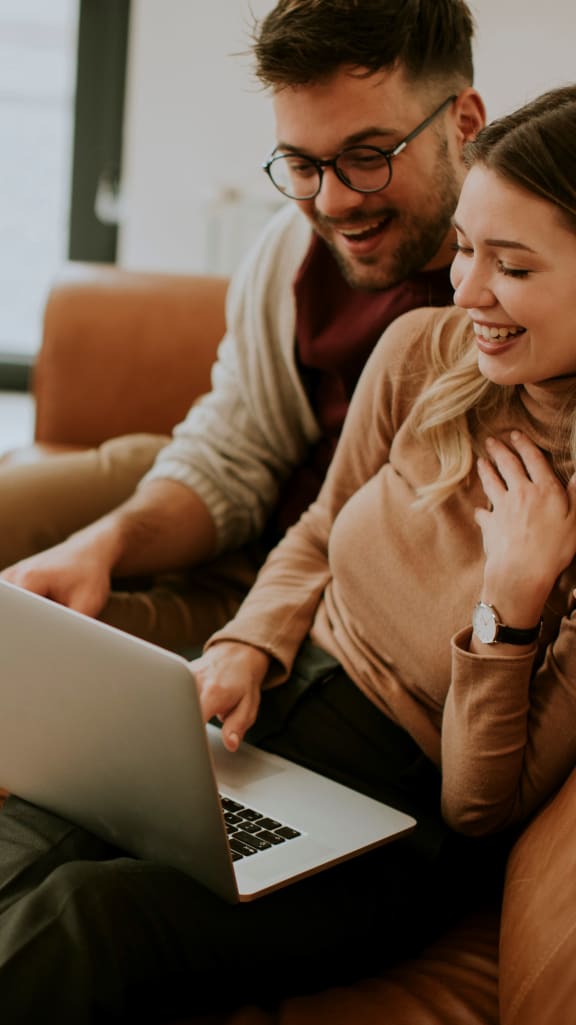 Couple Sitting on Sofa Looking at Laptop Together Smiling