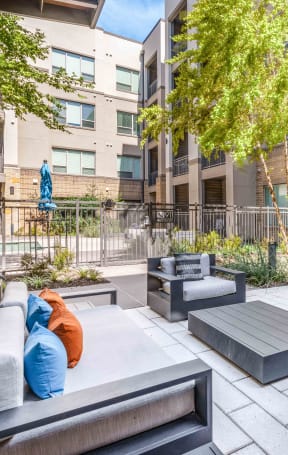 an outdoor lounge area with couches and tables in front of an apartment building