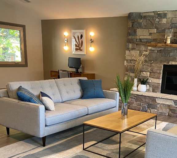 A living room with a stone fireplace and a grey couch.