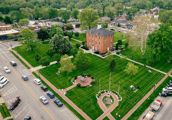 A park with a red brick building and a circular garden with a cross in the middle.