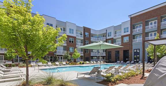 A pool area with a tree and chairs in front of apartment buildings.