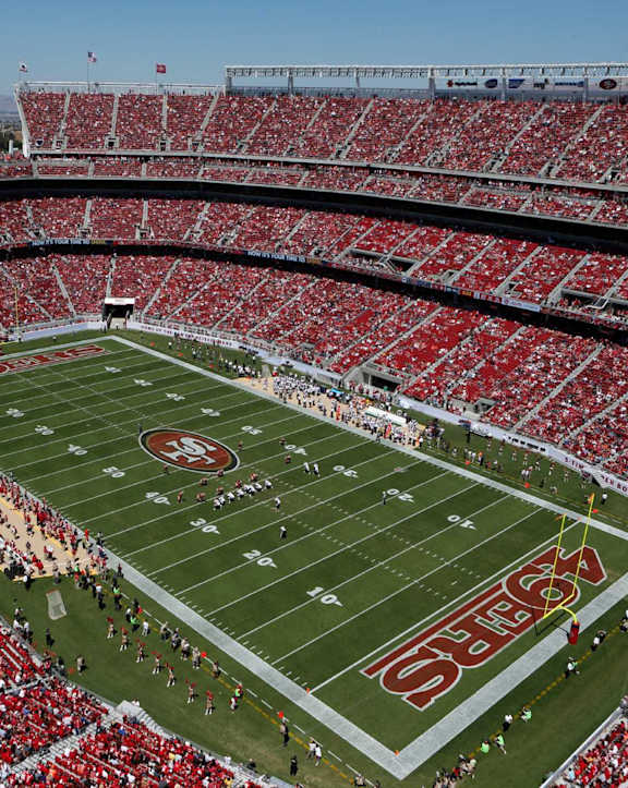 A stadium full of red seats with a football game taking place.