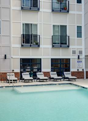 A pool in front of a white building with black railings.