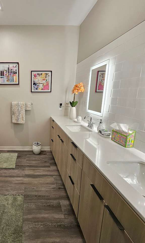 A modern bathroom with wall to wall cabinets and double sinks with illuminated mirror.