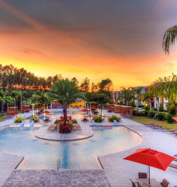A beautiful outdoor swimming pool area with red umbrellas and lounge chairs.
