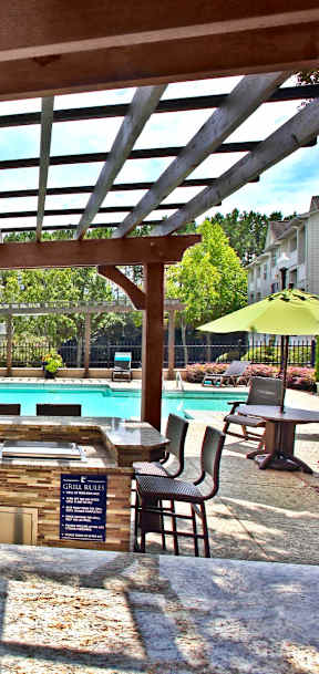 A wooden pergola over a patio with a pool in the background.