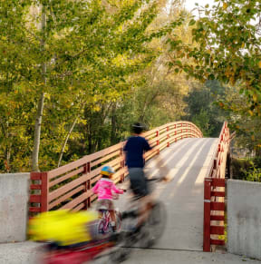 Parent and Child Biking in Park Across Bridge