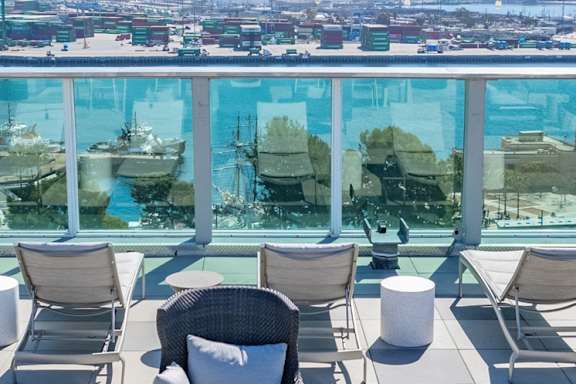 A patio with chairs and a table overlooking a pool and cityscape.