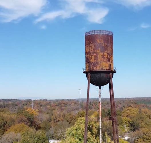 Rusty water tower in Spartanburg, standing against autumn trees, reflecting its industrial past.