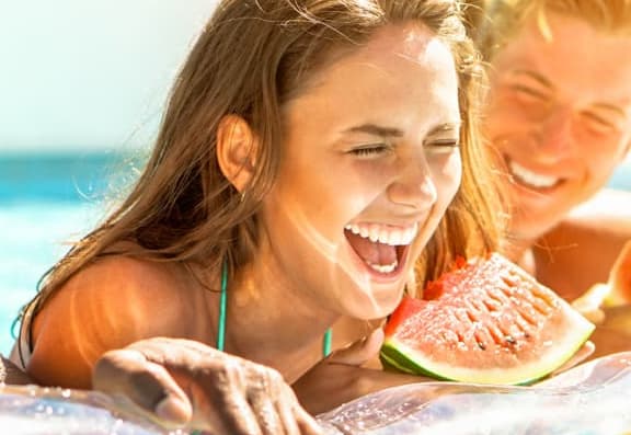 lifestyle image of three people at the pool eating watermelons 