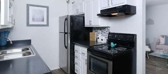 Fifteen 50 apartments Las Vegas kitchen with black and silver appliances, white cabinets, and modern black countertops and greyscale tile backsplash