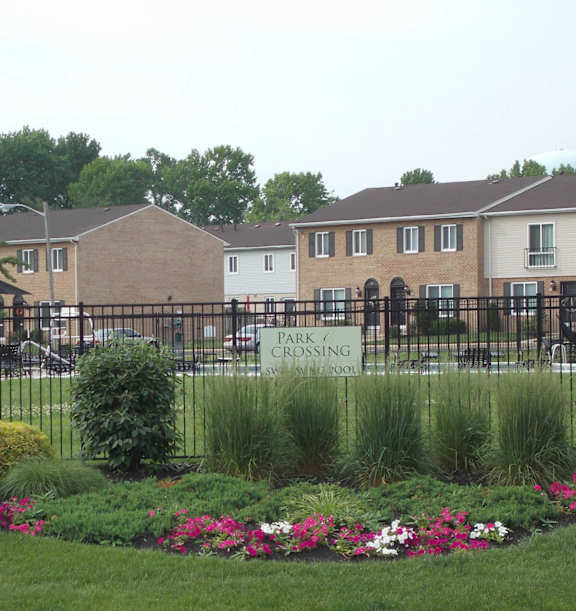 A park crossing sign is on a fence in front of a residential area.