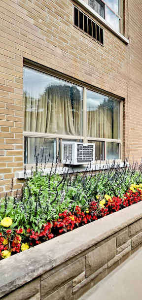 a side view of a brick building with a flower garden on the sidewalk