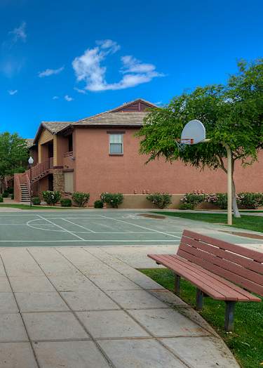 A basketball court with a bench on the side and two houses in the background.