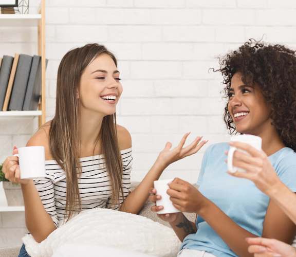 three women sitting on a couch drinking coffee and talking