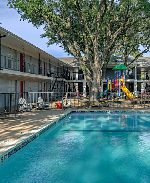 A swimming pool in a courtyard surrounded by red lounge chairs.