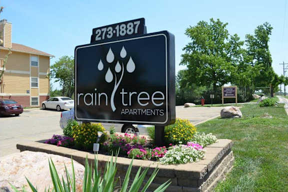 A sign for Rain Tree Apartments is displayed in front of a building.