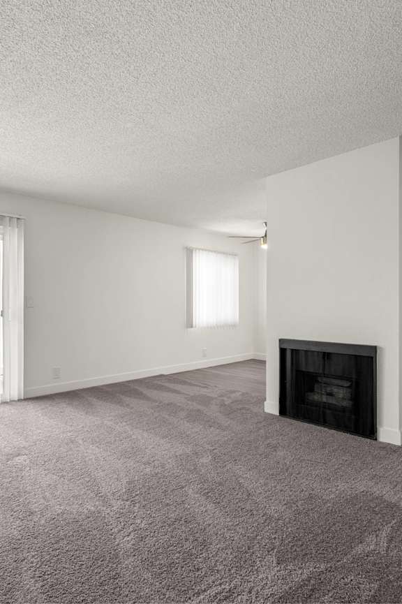 A large, empty room with a fireplace and carpeted floor.
