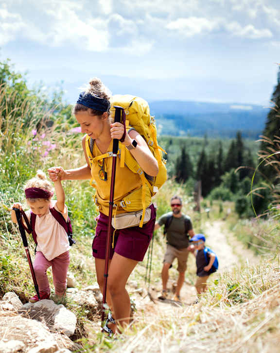 A family of hikers, including a child, are walking on a trail in a natural setting.
