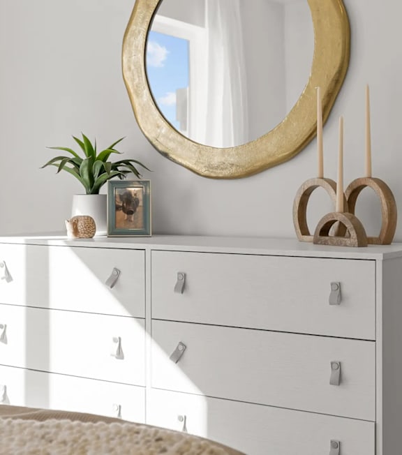 A white dresser with a round mirror and a plant on top.