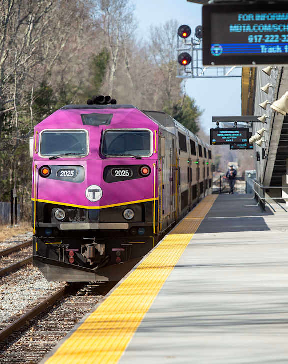 A pink train is on the tracks at the station.
