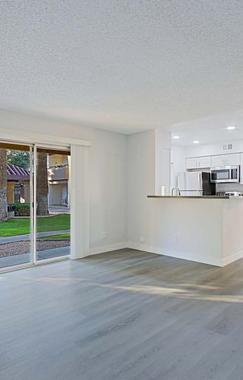 A spacious, empty room with a kitchen area visible through the glass door.
